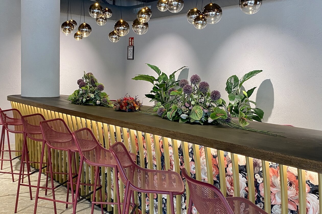 Langer Business-Tisch mit Holzplatte, goldenen Lamellen, Blumenstoff und roten Hochstühlen im Café der Confiserie Gordani Lasch in Karlsruhe