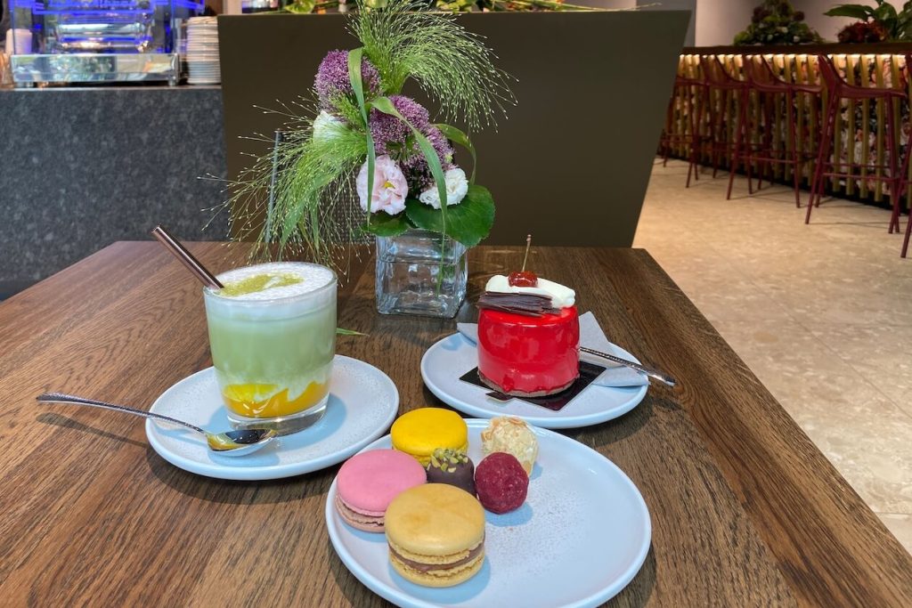 Iced Matcha Mango, rotes Kirsch-Törtchen, Macarons und Pralinen auf einem Holztisch in der Confiserie Gordani Lasch in Karlsruhe