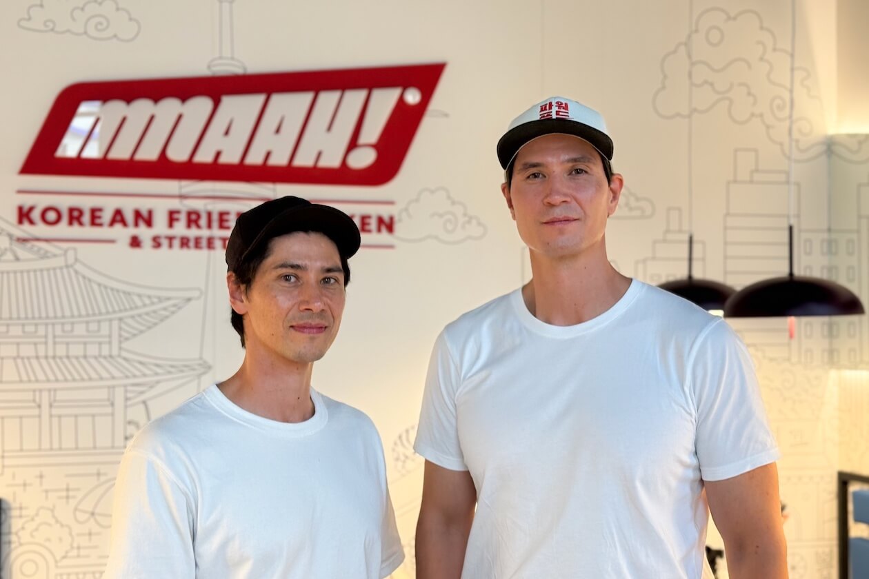 Die Mmaah!-Gründer Sebastian Sung Chu und Andreas J. Young in weißen T-Shirts vor dem Mmaah!-Logo im Store in Karlsruhe