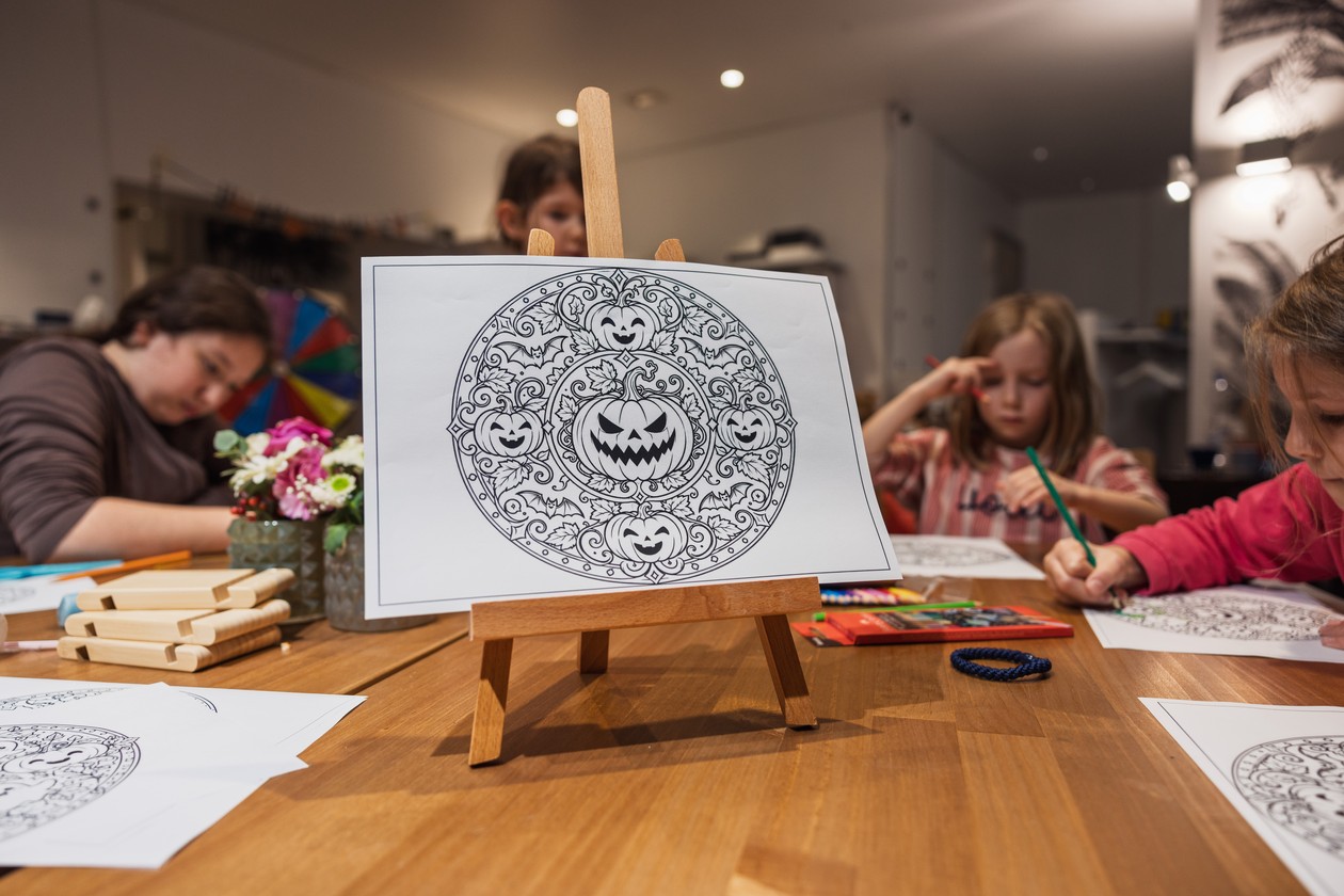 Kinder malen am Tisch Mandalas aus, vorne ein Kürbis-Mandala auf einer Mini-Staffelei